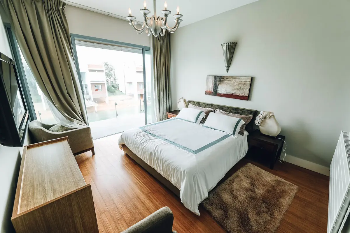 A bedroom with soft olive curtains and a made bed